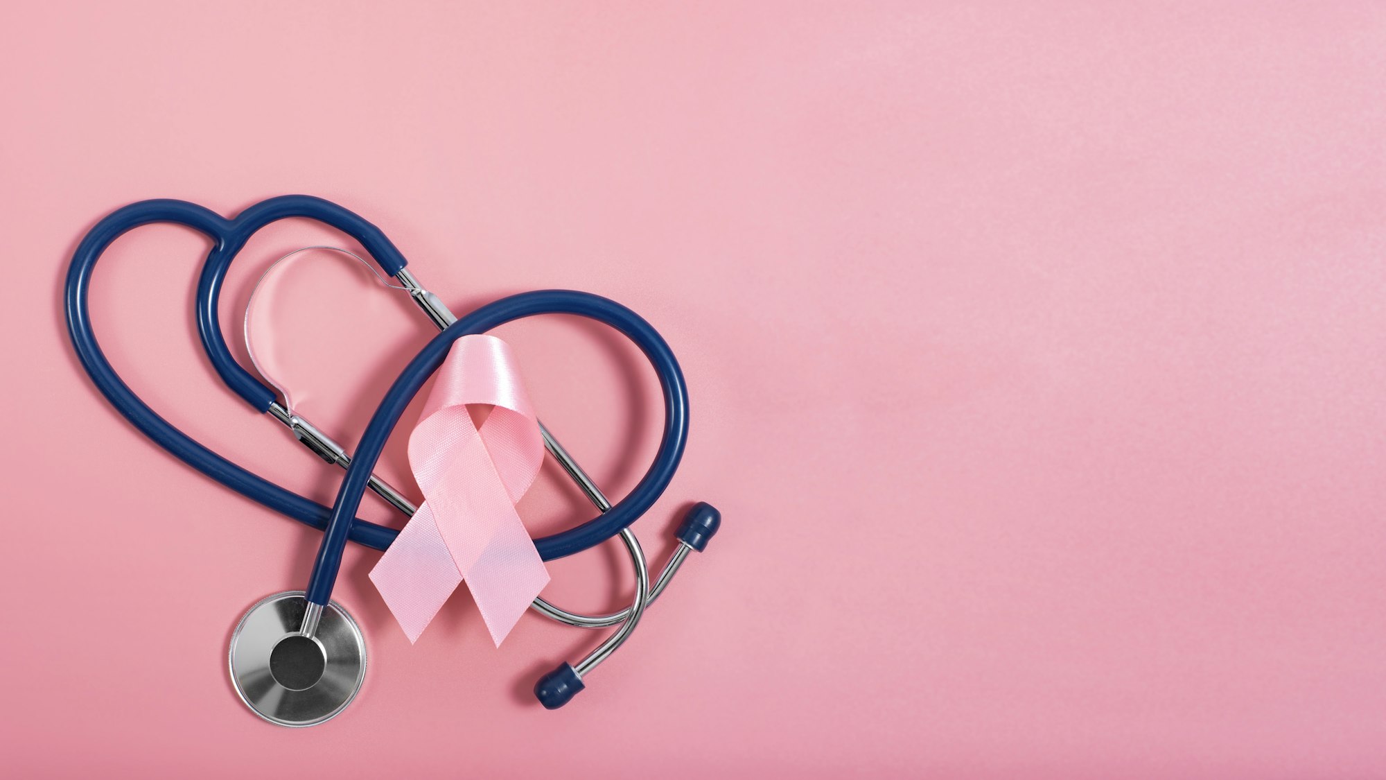 Stethoscope and pink ribbon on pink background as breast cancer awareness symbols. Flat lay view
